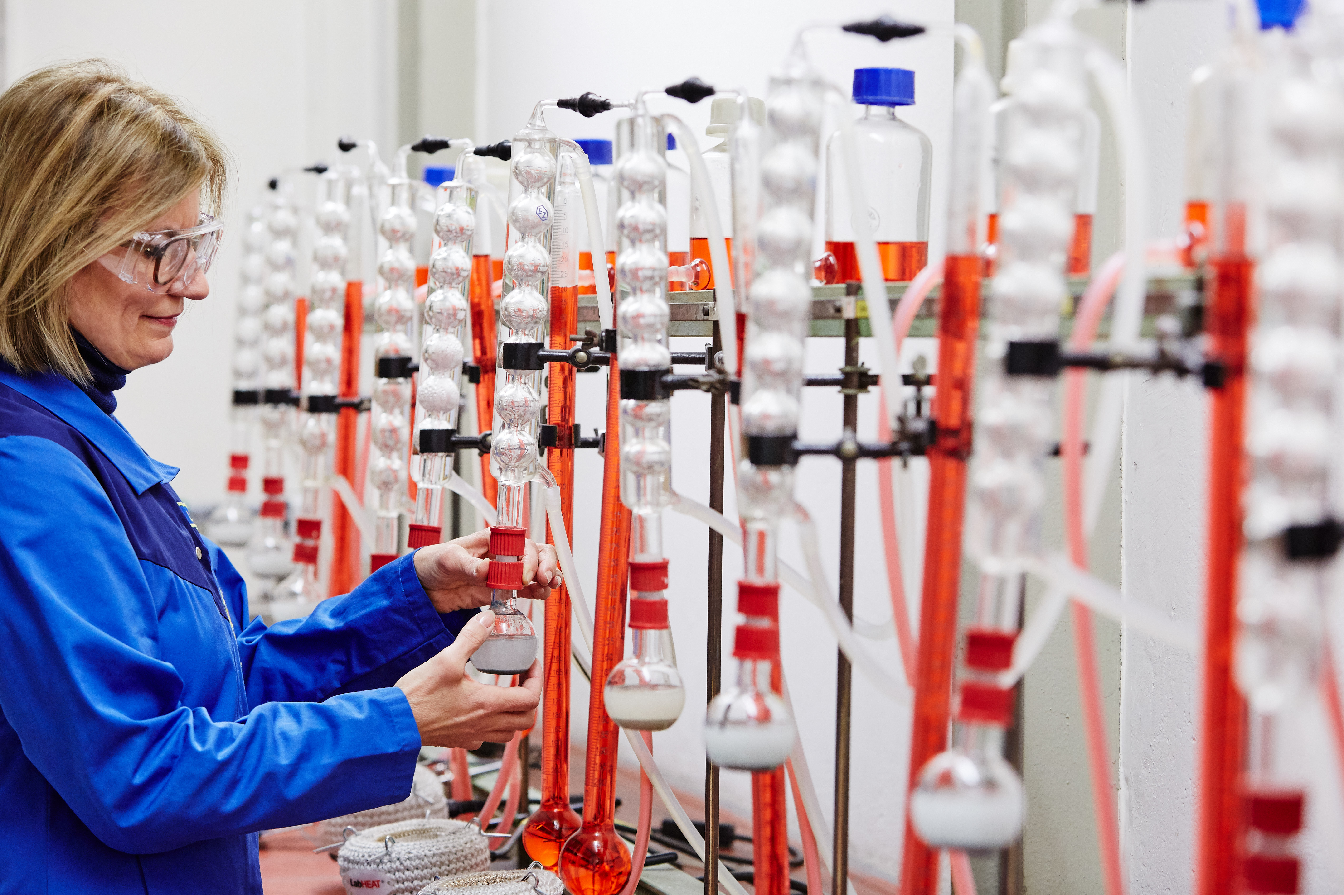 Eine Frau im Laborkittel füllt aus einer Glas-Apparatur in einem Labor eine Flüssigkeit ab.