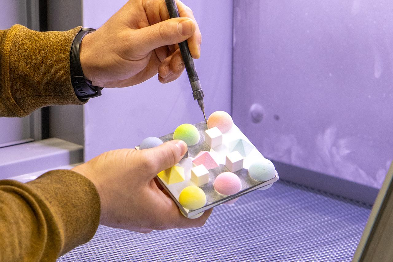 Eine Hand hält eine Art elektronische Nadel, die in bunte Kugeln sticht