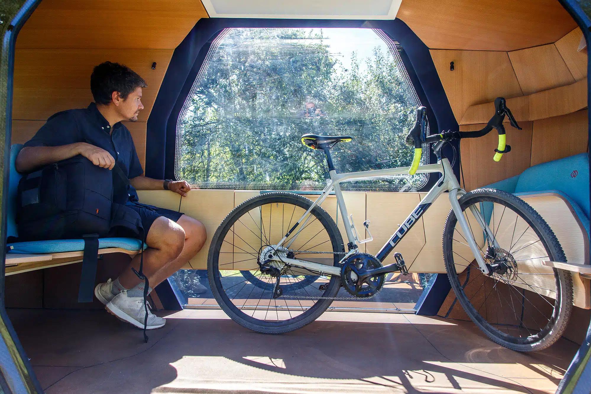 Mann mit Fahrrad sitzt in selbstfahrender Kabine auf Schienen, die einem kleinen Zug-Wagon ähnelt