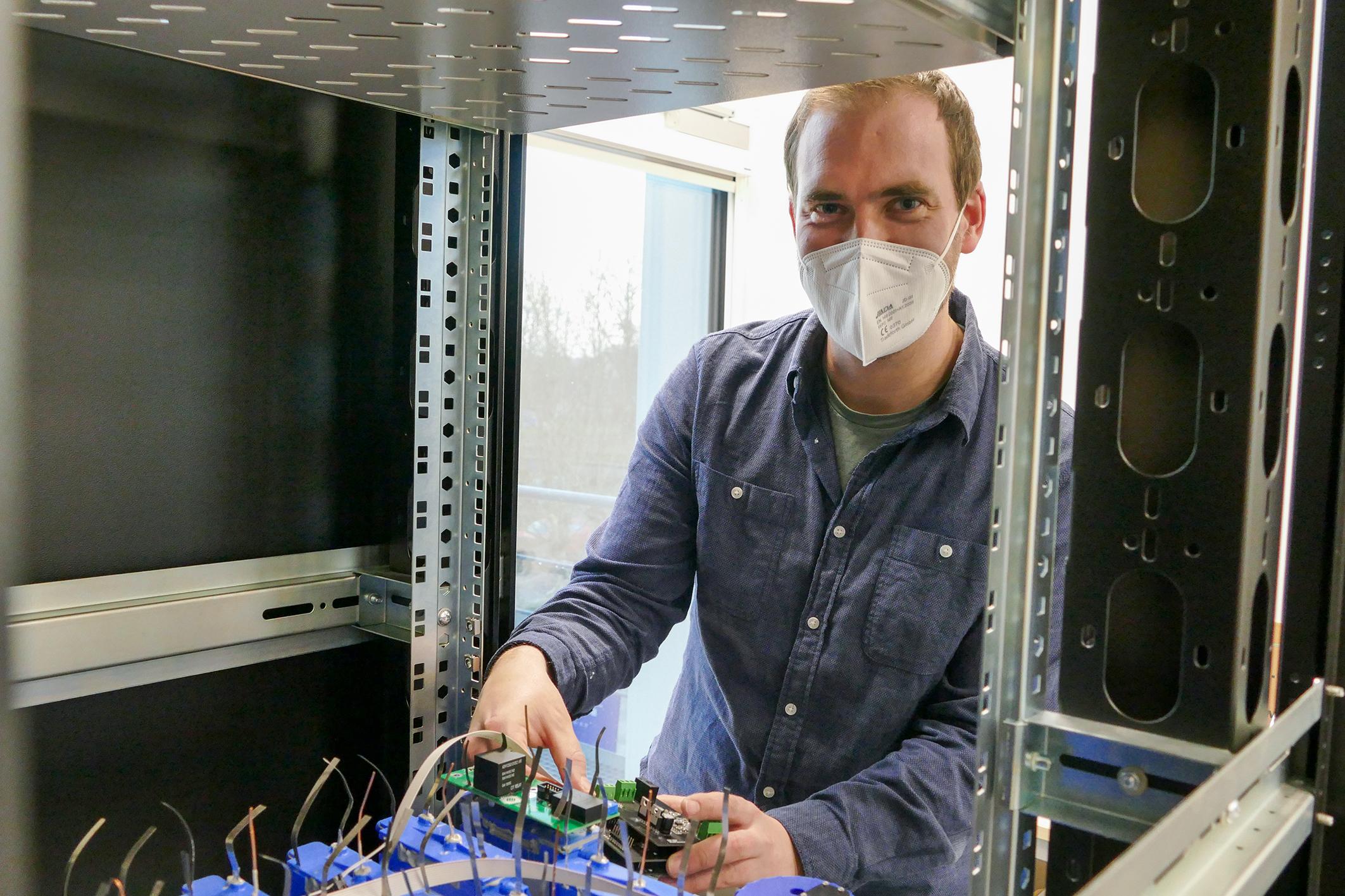 Mann mit FFP2-Maske arbeitet an elektrischen Verschaltungen