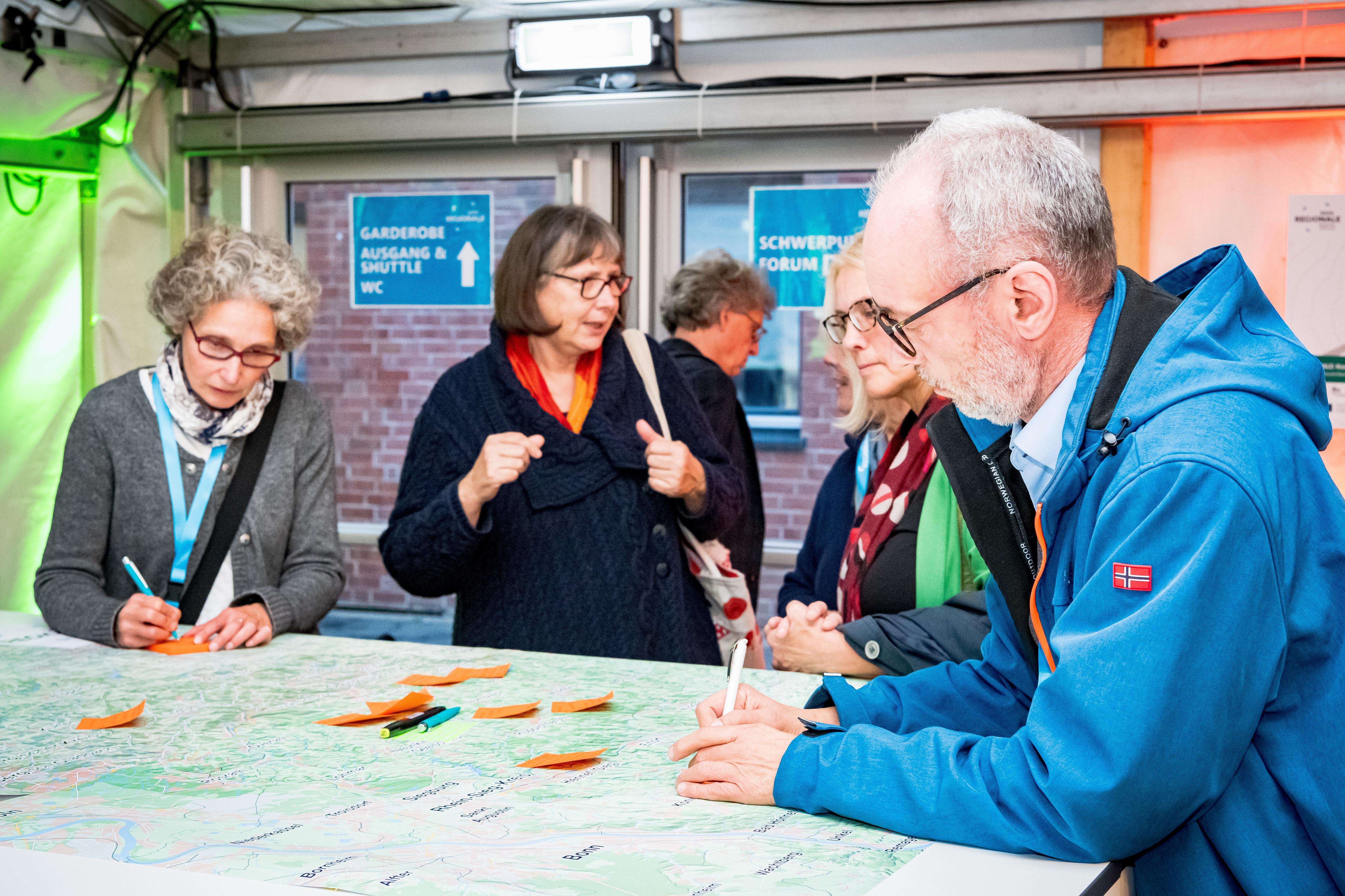 Mehrere Menschen stehen an einem Tisch und schreiben etwas auf Post-its.