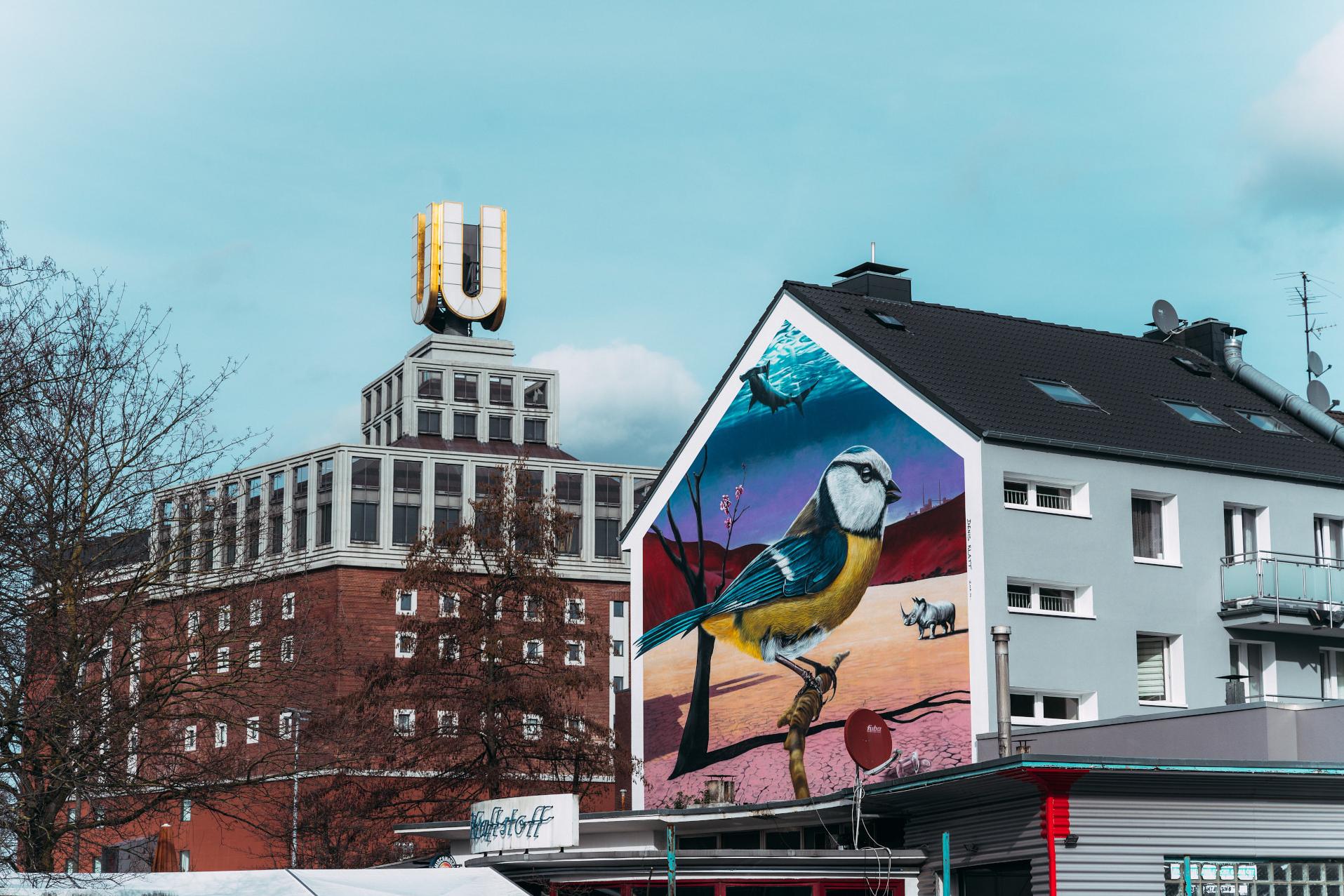 Rechts im Bild ist ein Haus zu sehen. Im Hintergrund links sieht man das Dortmunder-U, ein Gebäude mit einem großen U auf dem Dach.
