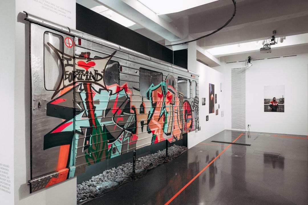 Man sieht eine Ausstellung, in der Street-Art auf einem Bahnwagon zu sehen ist.