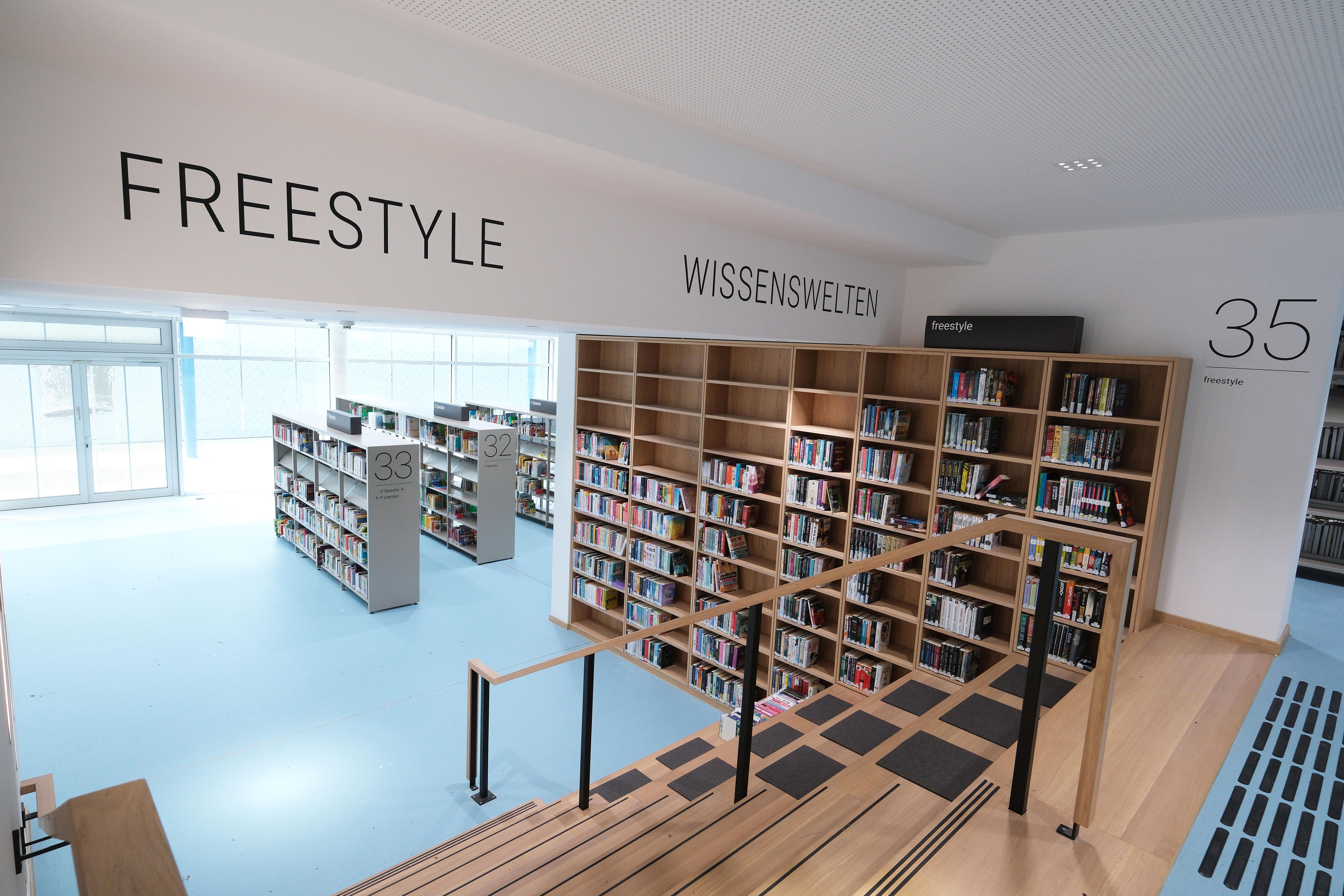 Es wird eine Bücherei von innen abgebildet. Es sind viele Bücher und eine Treppe zu sehen.