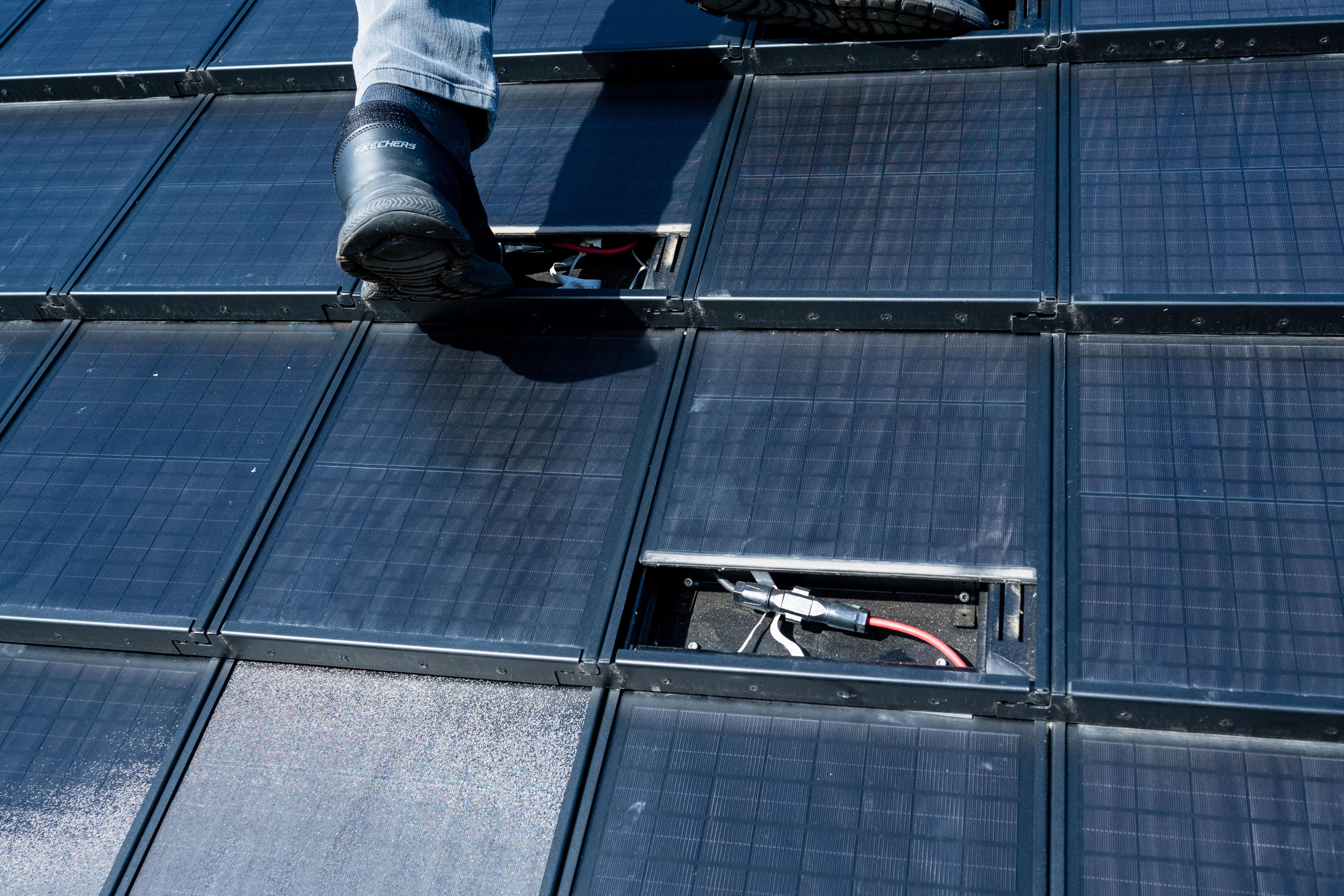 Ein mit Solarpaneln gedecktes Dach. Eine Person klettert auf Stufen zwischen den Panels nach oben.