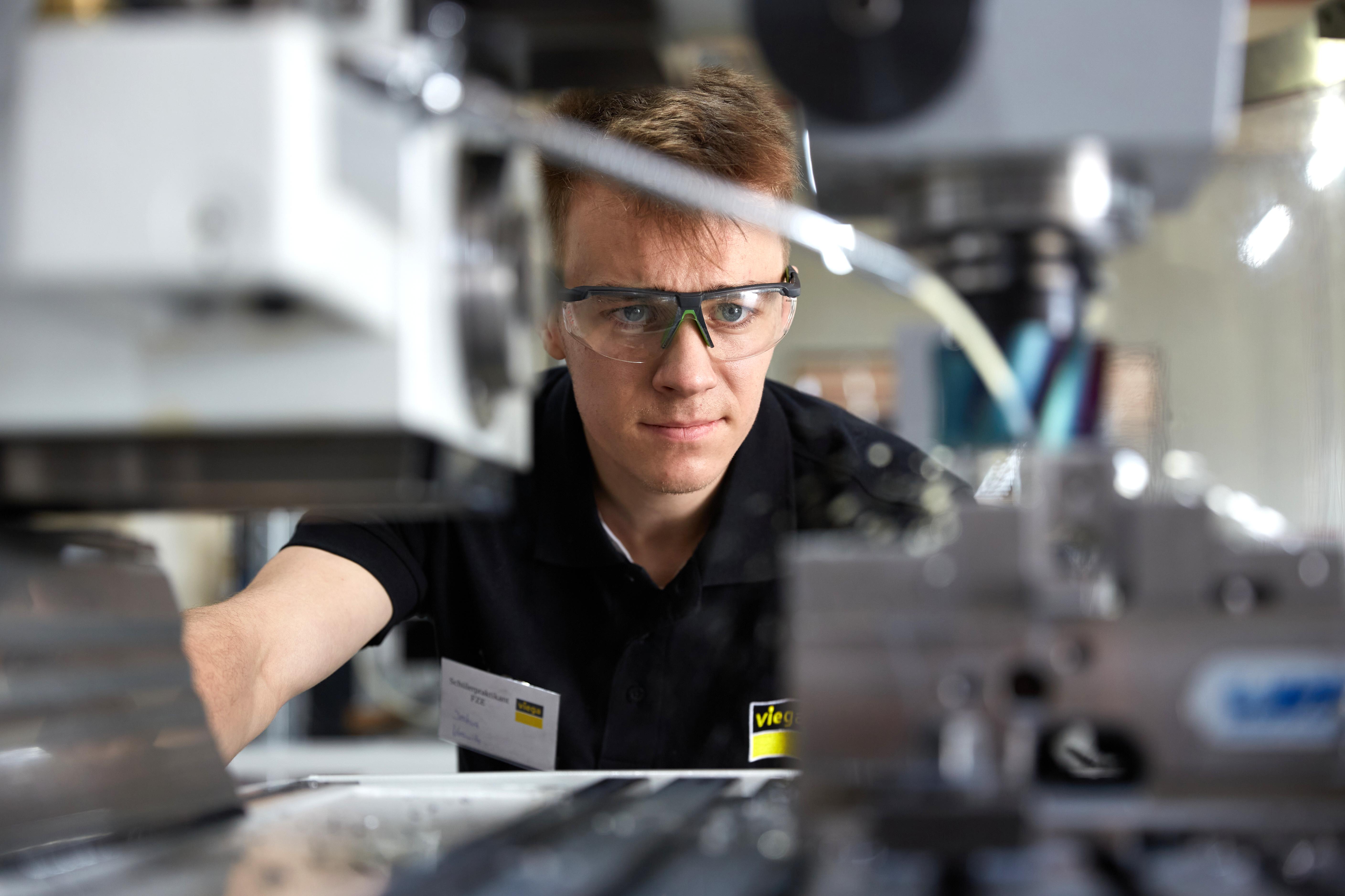 Ein junger Mann mit Schutzbrille arbeitet an einer Maschine.