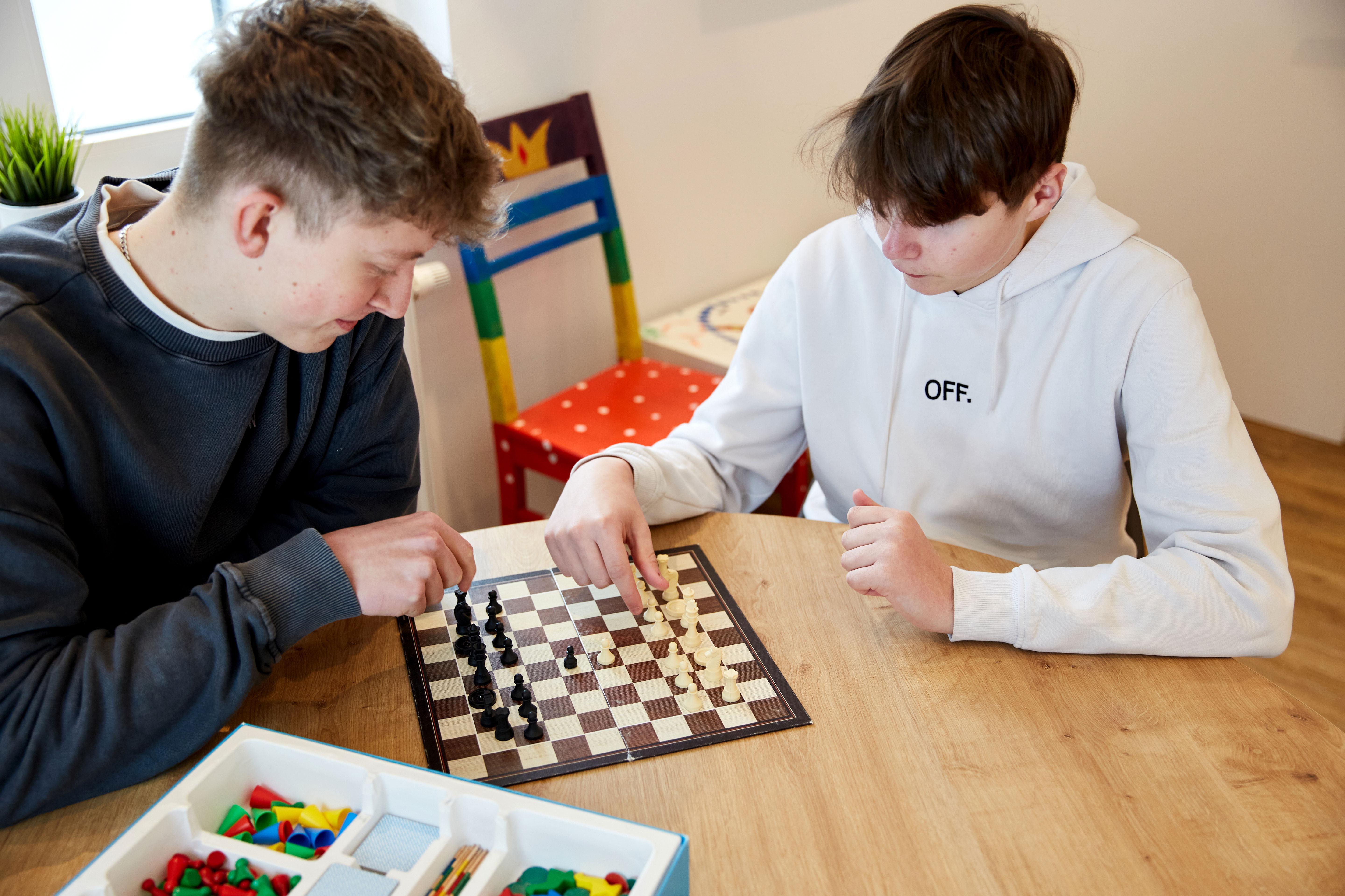 Zwei jugendliche Jungen sitzen an einem Holztisch und spielen Schach.
