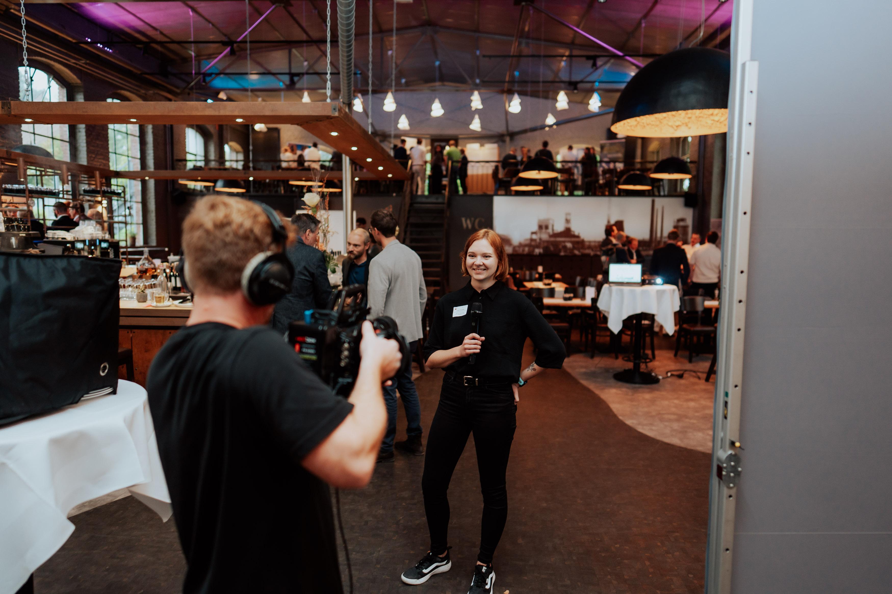 Eine Person mit Kamera und Ton interviewt eine andere Person, die ein Mikrofon in der Hand hält. 
