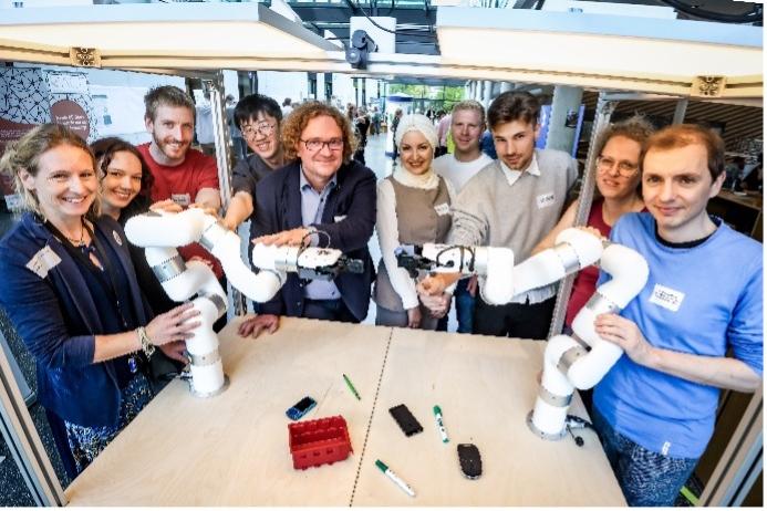 Gruppe an Menschen steht um einen Tisch mit zwei Roboterarmen