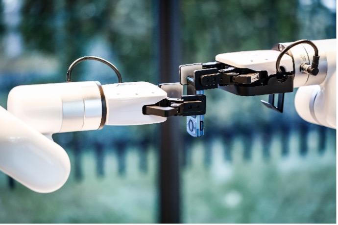 Zwei Roboterarme greifen gemeinsam einen Gegenstand.