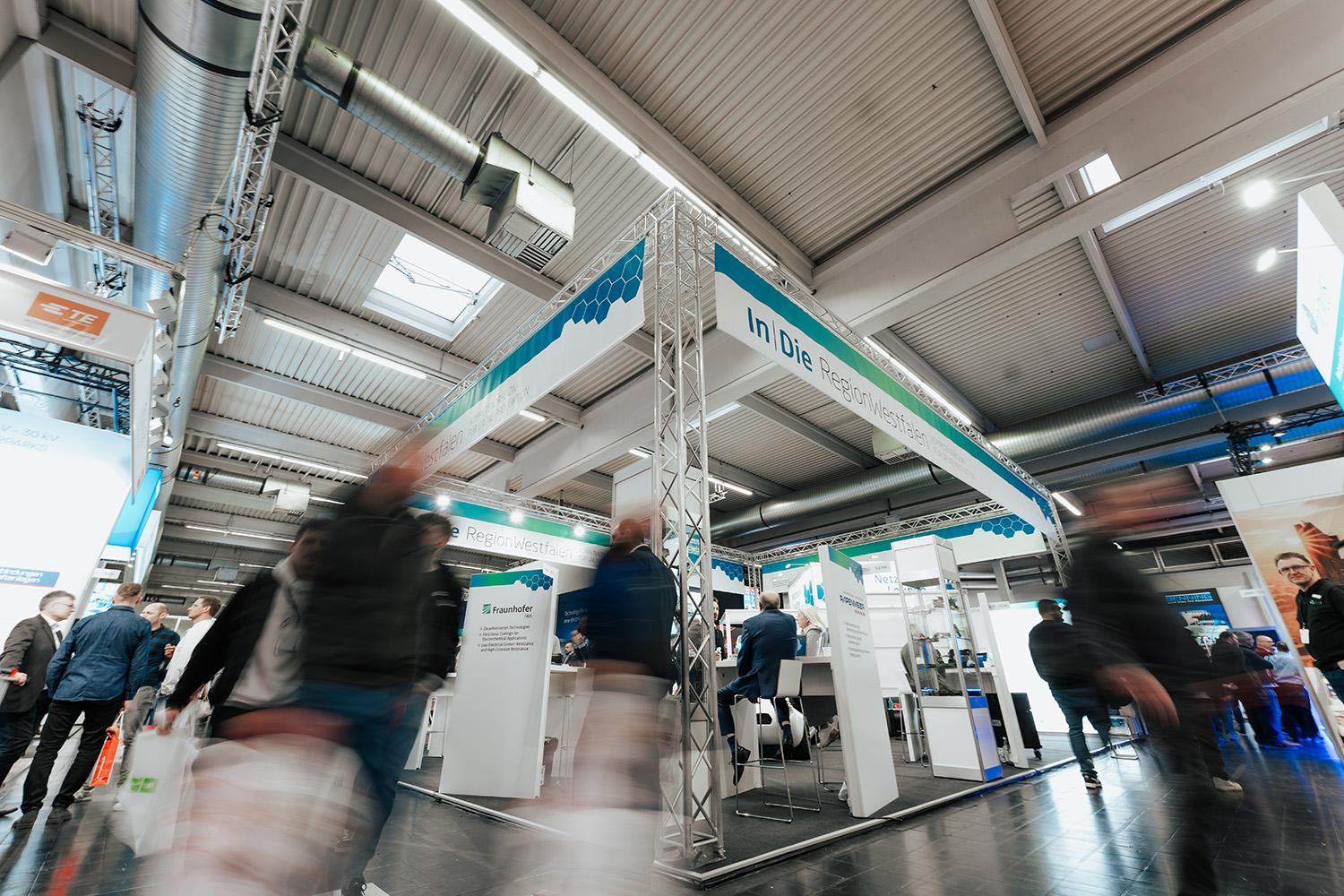 Aufnahme eines Messestandes der In|DieRegionWestfalen. Personen sind nur verschwommen sichtbar. 