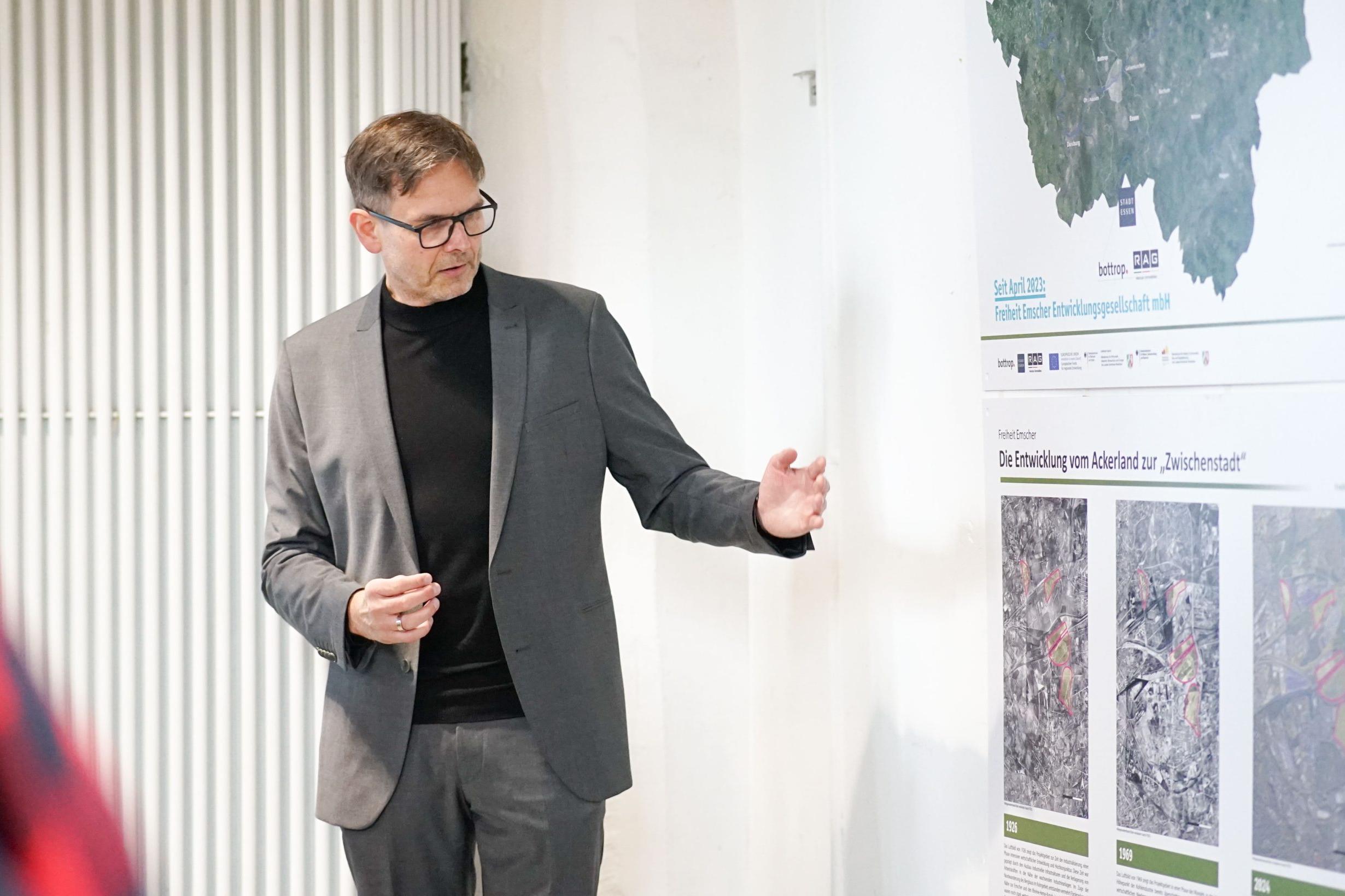 Ein Mann zeigt etwas auf Plakaten, die an der Wand hängen.