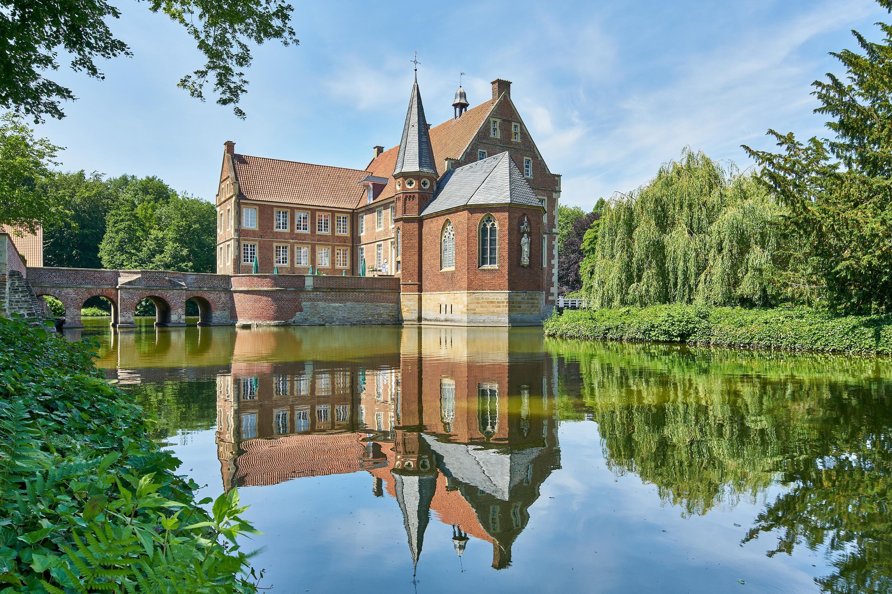 Eine kleine Burg vor einem See im Sonnenschein.