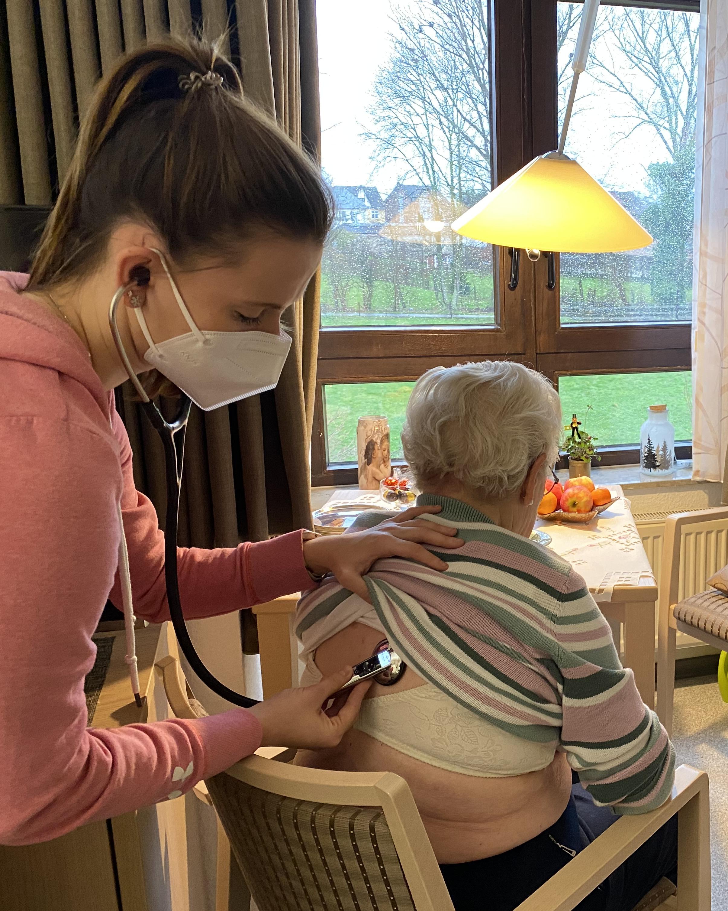 Frau mit FFP2-Maske hört älterer Frau mit Stethoskop den Rücken ab