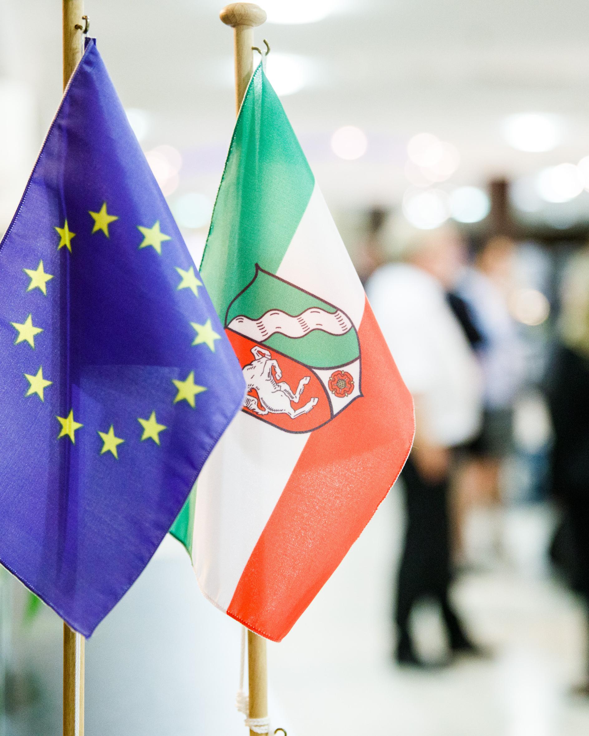 Eine EU- und eine NRW-Flagge aufgehängt an Aufstellern auf einer Veranstaltung