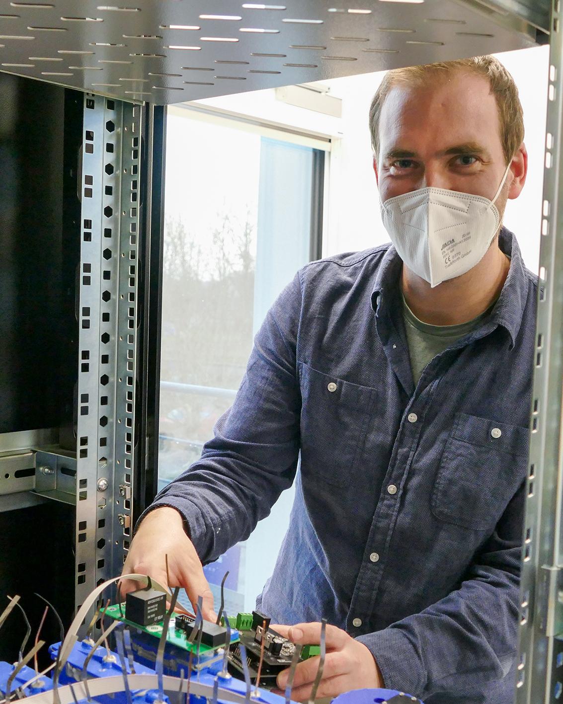 Mann mit FFP2-Maske arbeitet an elektrischen Verschaltungen