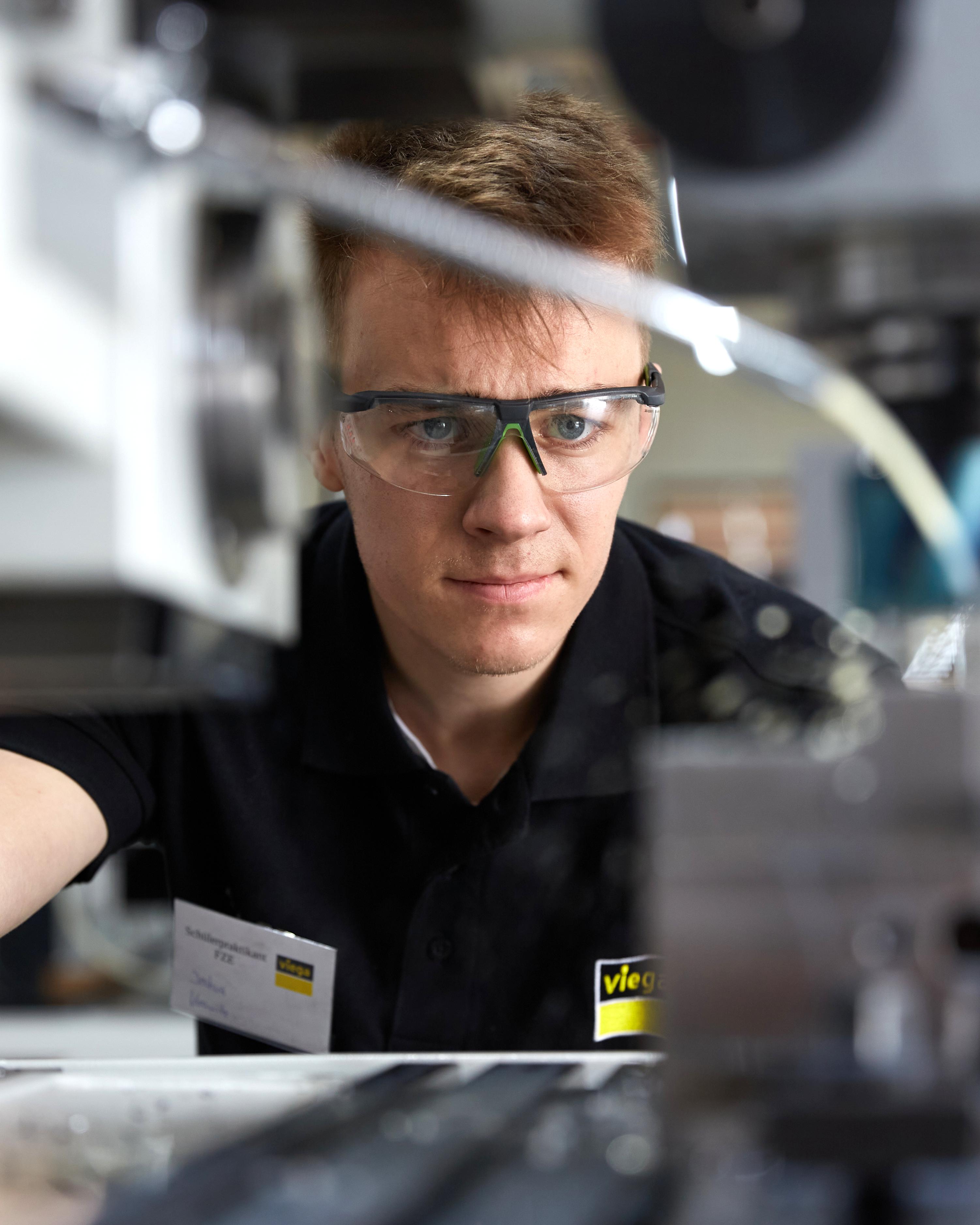 Ein junger Mann mit Schutzbrille arbeitet an einer Maschine.