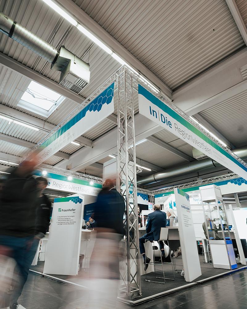 Aufnahme eines Messestandes der In|DieRegionWestfalen. Personen sind nur verschwommen sichtbar. 