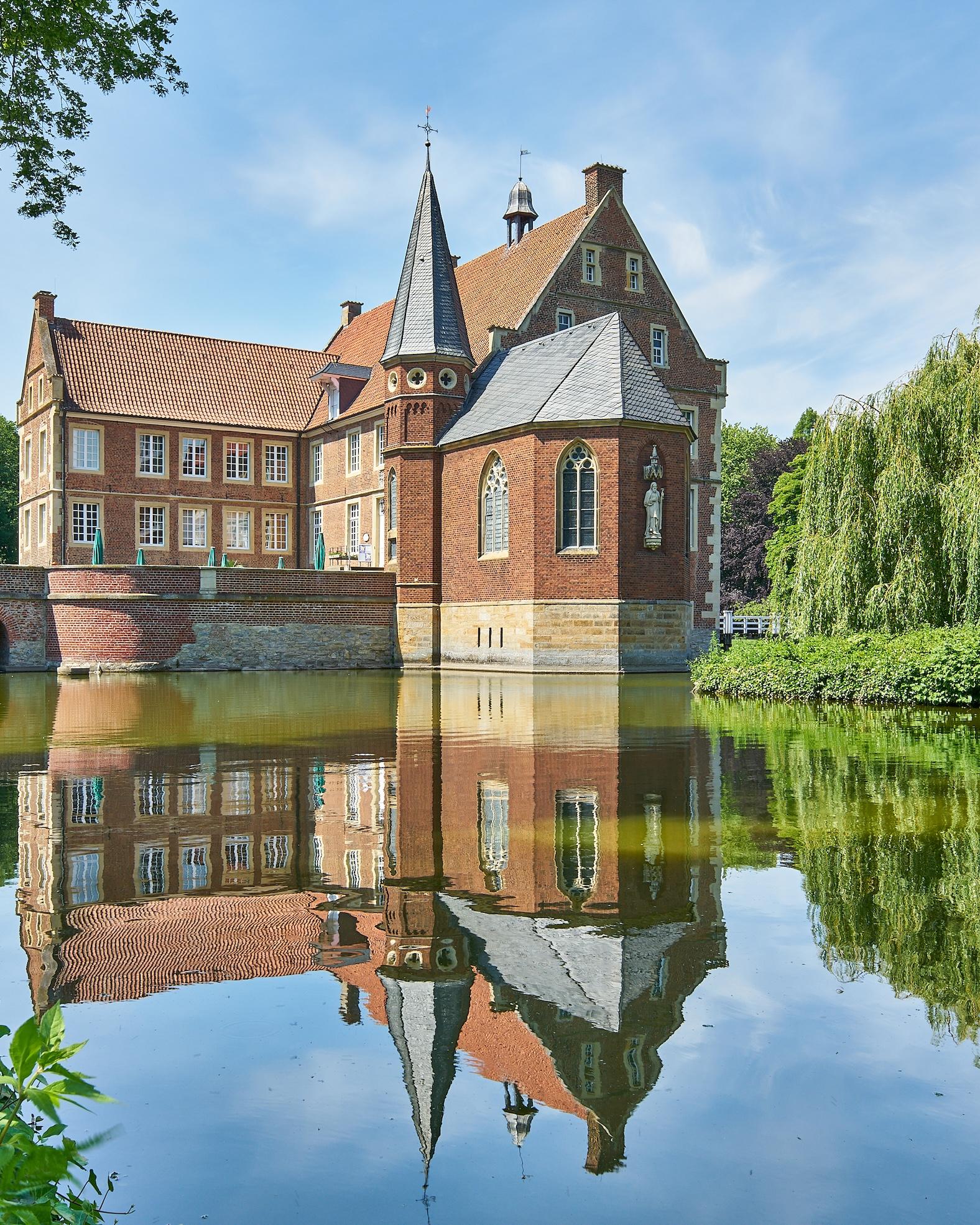 Eine kleine Burg vor einem See im Sonnenschein.
