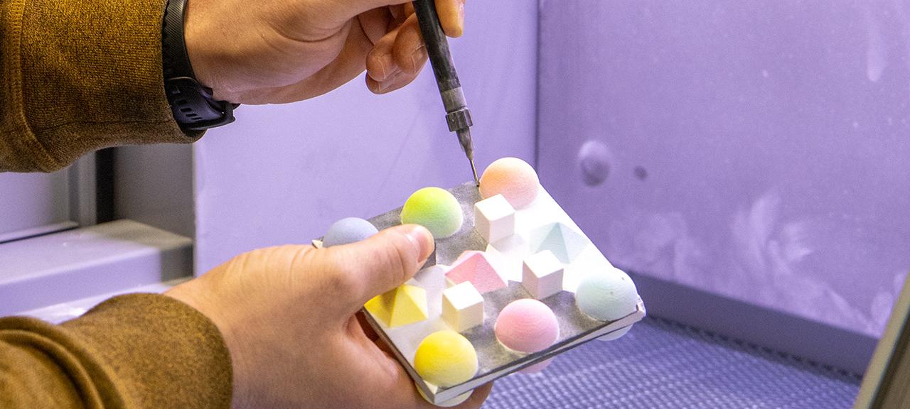 Eine Hand hält eine Art elektronische Nadel, die in bunte Kugeln sticht