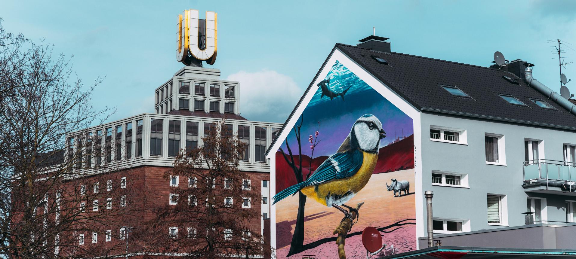 Rechts im Bild ist ein Haus zu sehen. Im Hintergrund links sieht man das Dortmunder-U, ein Gebäude mit einem großen U auf dem Dach.