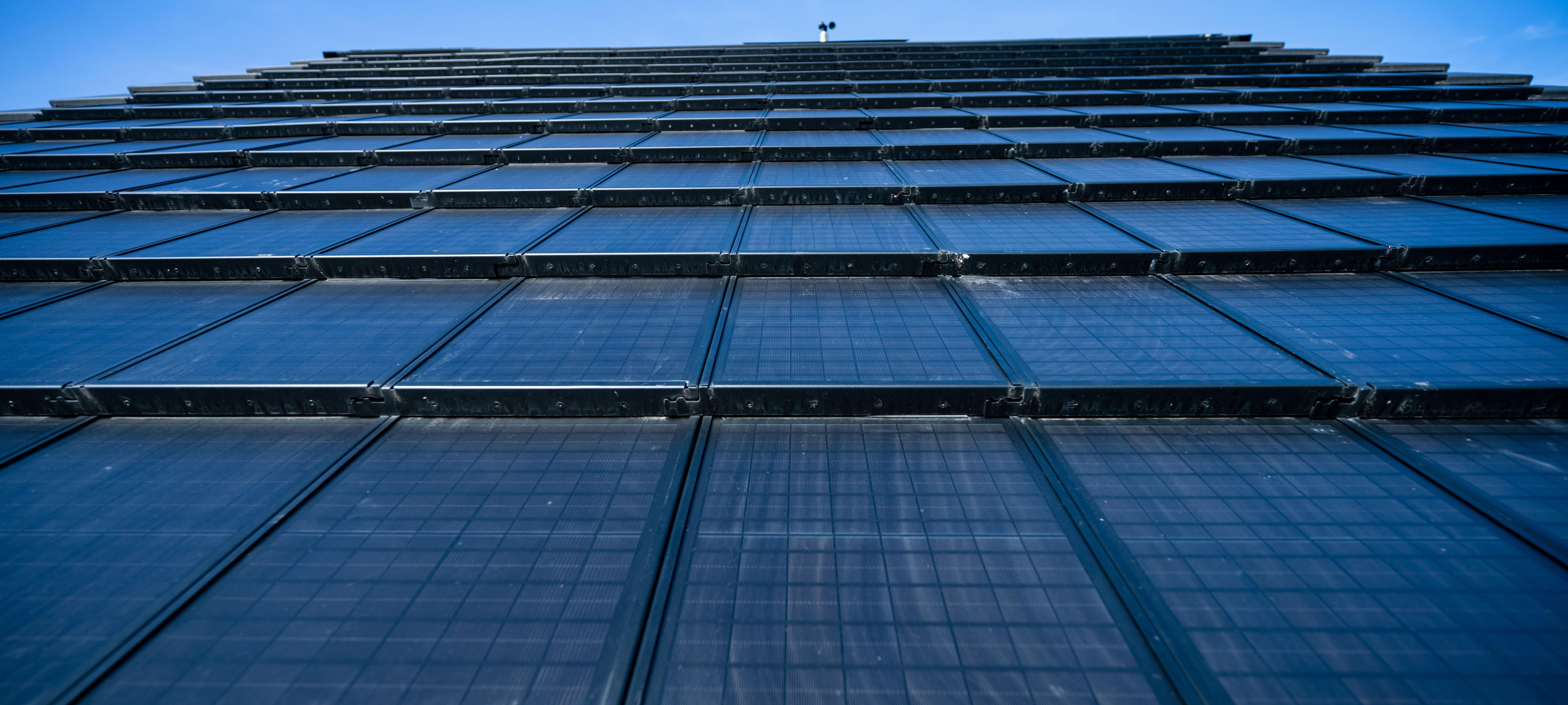 Eine mit Solarpanels gedeckte Wand ragt in einen blauen Himmel.