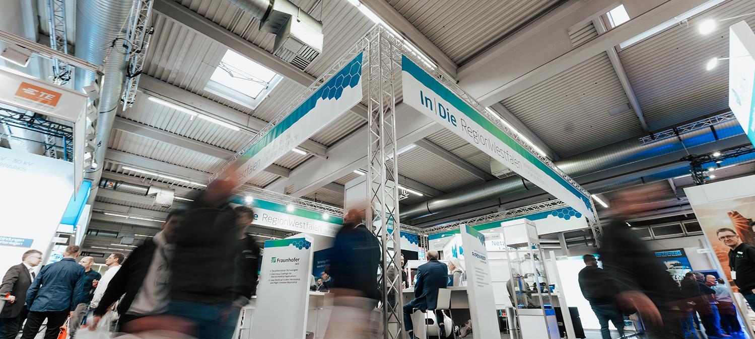 Aufnahme eines Messestandes der In|DieRegionWestfalen. Personen sind nur verschwommen sichtbar. 